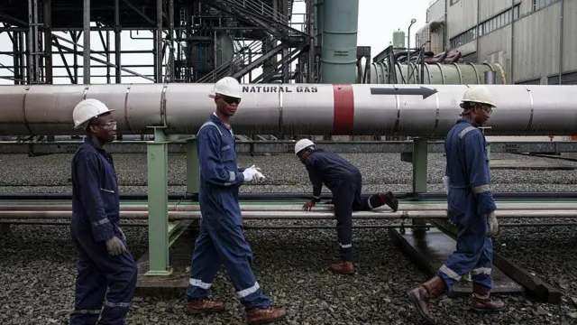 Gas workers dress for protective gear waka past large pipeline labelled 'natural gas'.