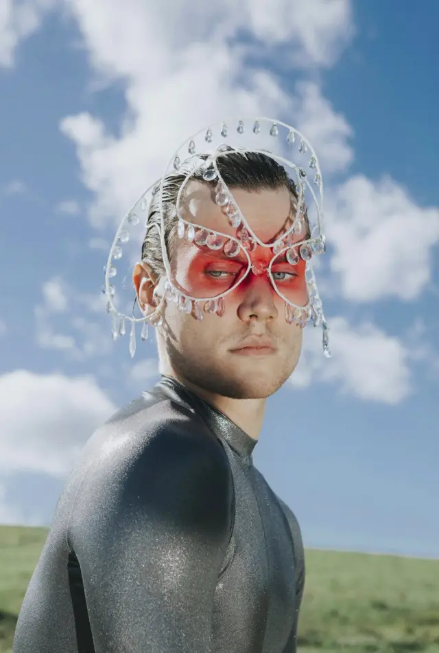 A fashion model poses with red face make-up and crystal head decorations