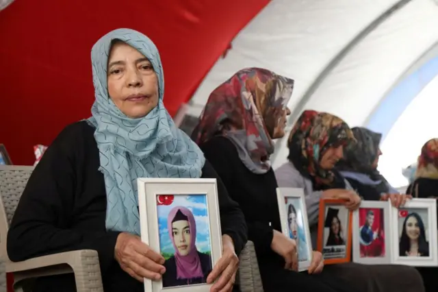 Ellerinde kız çocuklarının çerçeveli fotoğraflarını tutan anneler sırayla oturmuş. 