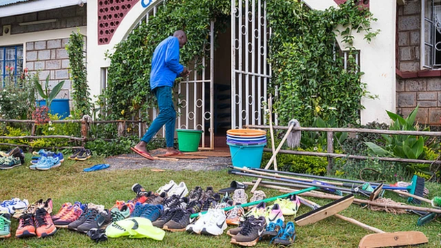 General scene of camp entrance, shoes littered on grass next to mops and brooms