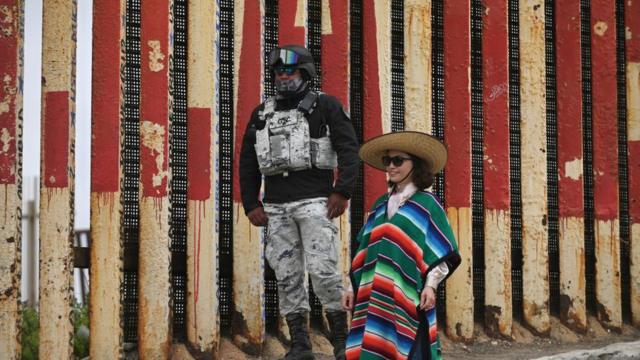 A Chinese tourist is dressing in traditional Mexican costume as she poses with a member of Mexico's National Guard at the site of the US-Mexico border construction in Playas de Tijuana, Mexico, on Friday, June 9, 2023.