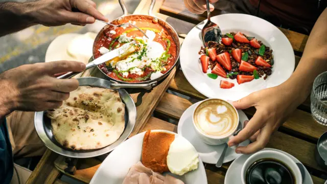 Przy stoliku na zewnątrz serwowany jest posiłek z granolą z truskawkami, chlebem pita i cappuccino. 