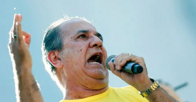 Foto de Silas Malafaia empunhando um microfone e usando uma camisa amarela
