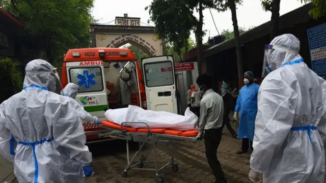 দিল্লির নিগমবোধ শ্মশানঘাটে একজন করোনা রোগীর দেহ নিচ্ছেন পিপিই-পরিহিত তার আত্মীয়স্বজনরা
