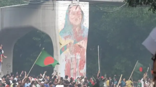 মেট্রোরেলের একটি পিলারে হাতে আঁকা শেখ হাসিনার ছবির ওপর লাল রংয়ের ছিটে। নিচে পতাকা ও লাঠি হাতে বিক্ষুব্ধ মানুষের ভিড়। ফাইল ছবি
