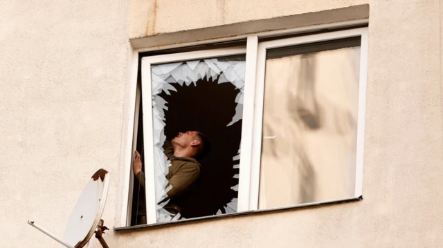 Чоловік у вікні з розбитим склом після масштабної атаки на Київ 