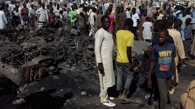 People gather at the site of the Kano bomb attacks