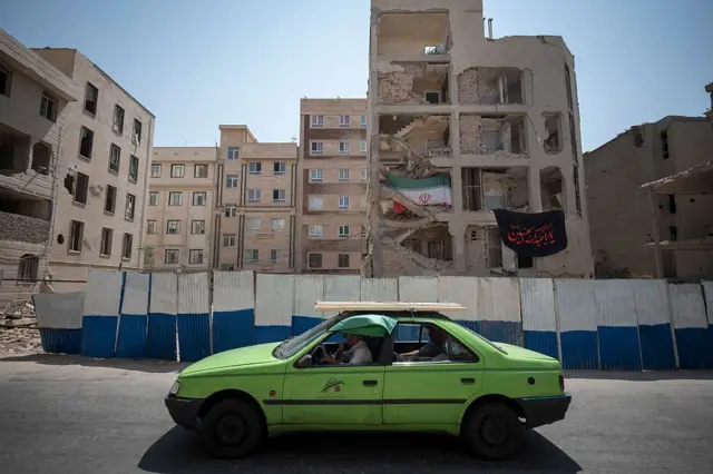 ইরায়েলের হামলায় ক্ষতিগ্রস্ত একটি ভবনে ঝুলছে ইরানের পতাকা