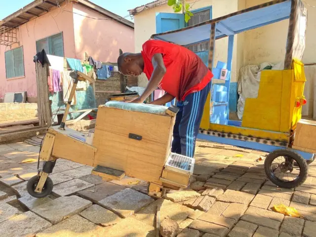Samuel Aboagye dey work on one of de tricycles