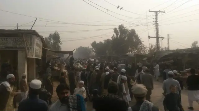 انبوه مردان در بازار اردوگاه شمشتو با لباس‌های محلی و کلاه‌های سنتی 