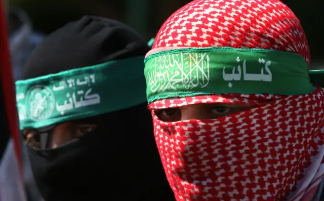 Abu Ubaida usando um keffiyeh vermelho na cabeça que mantémbwin é fiavelidentidadebwin é fiavelsegredo