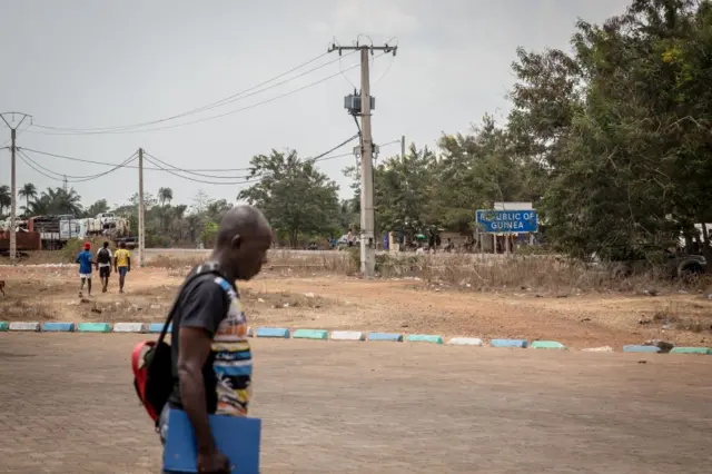Un homme passe devant un panneau indiquant la République de Guinée, qui marque la frontière avec la Sierra Leone. 