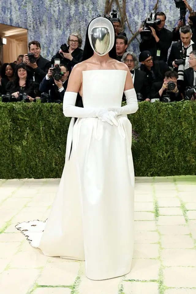 Katy Perry beyaz bir elbise giyiyor. Yüzü aynalı bir başlıkla gizlenmiş.