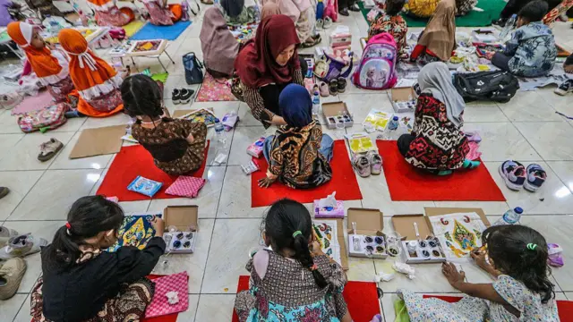 Little girls sitting on the floor painting, with teachers helping them