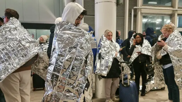 Passengers for Gatwick Airport after di evacuation. Dem dey covered in silver foil heat warmers.