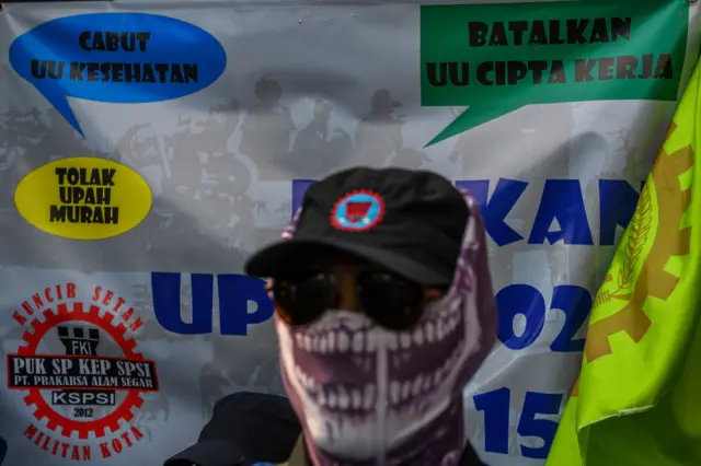 Seorang pengunjuk rasa yang tergabung dalam Konfederasi Serikat Pekerja Seluruh Indonesia (KSPSI) berdiri di depan spanduk saat aksi di Patung Kuda Arjuna Wijaya, Jakarta Pusat, Kamis (14/9/2023).
