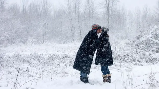 Two people kiss in a forest while snow is falling