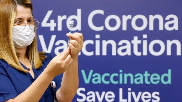 Врач со шприцем на фоне плаката, призывающего сделать четвертую прививку
