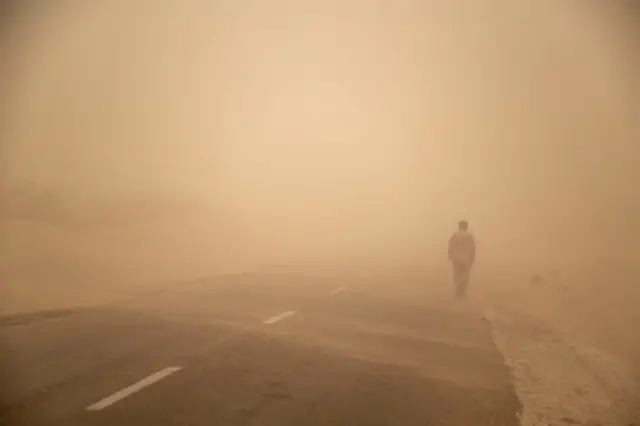 ۱۰ ژوئیه ۲۰۱۸، سیستان و بلوچستان، ایران. مردی در طوفان گرد و غبار در حال قدم‌زدن در امتداد جاده‌ای در سیستان و بلوچستان.