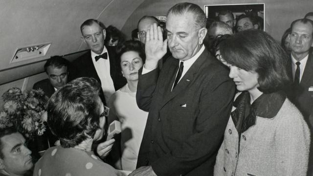 Vice-President Lyndon Baines Johnson (C) is sworn in as JFK's stunned widow stands by just two hours after he was shot