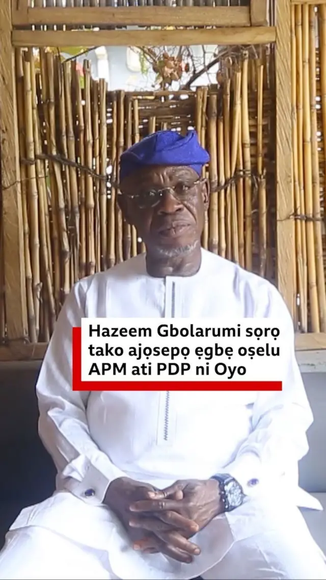 Amofin azeem Gbolarumi wọ asọ toke tilẹ funfun, o de fila asọ oke alawọ buluu, o joko sori aga, o lo awo oju, o si so ọwọ rẹ mejeeji papọ