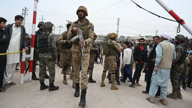 Kamuflaj üniformalı silahlı askerler ve yerel halktan insanlar yerel giysileriyle sokakta toplanmış