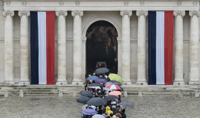 Visitors, many of them carrying umbrellas, stand close to the entrance of Les Invalides in Paris on 29 September 2019.