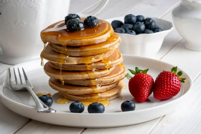 Un plato de panqueques cubiertos con jarabe y con frutas.