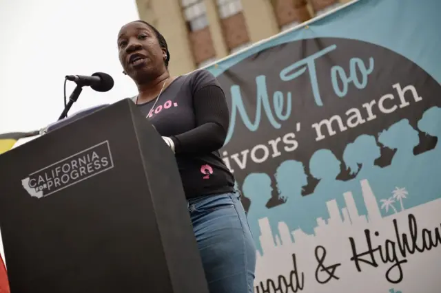 Tarana Burke discursando em frente a painel com hashtag 'Me Too'