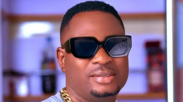 Ayoola Akinola Michael (Alayo Singer) o lo igo dudu, lo ẹgba ọrun,aṣọ alawọ eeru to wọ n han fẹẹrẹfẹ, o si n rẹrin-in muṣẹ.