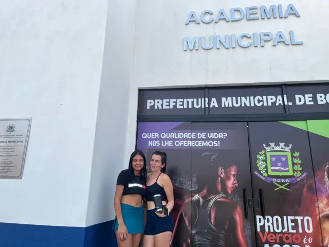 Duas amigas posando para foto em frente à fachada da academia municipal