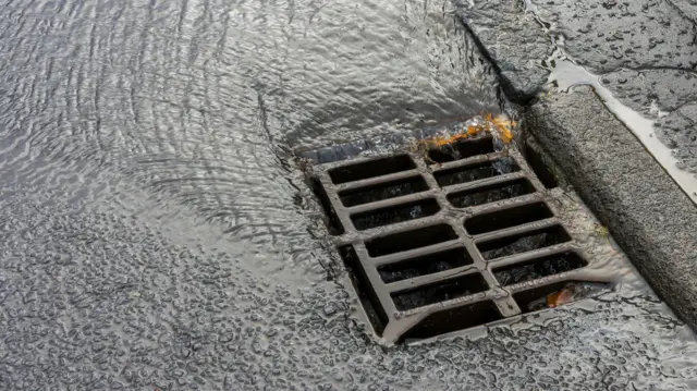 Фото решітки вуличного зливу, у який стікає вода