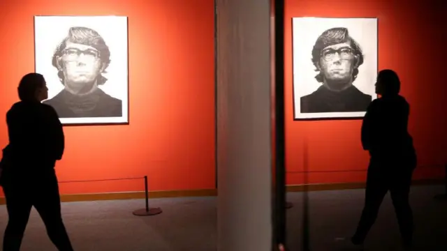 Seorang perempuan mengamati lukisan 'Keith Mezzotint' karya Chuck Close, dan bayangan dirinya serta karya seni tersebut terpantul di cermin.