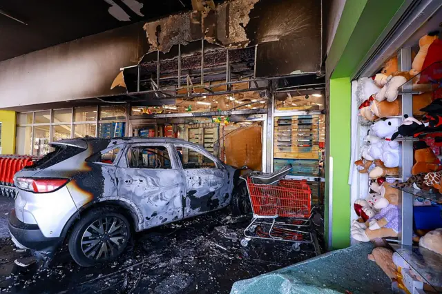 Sebuah mobil yang terbakar menabrak pintu masuk sebuah toko di pusat perbelanjaan pada 22 Februari 2026 di Guadalajara, Meksiko. Blokade jalan dan pembakaran kendaraan telah dilaporkan di beberapa bagian Meksiko sejak pagi hari.