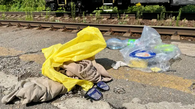 鉄道の線路のかたわらに、靴やめがね、衣服、ビニール袋に入った食べ物などがまとめて置かれている