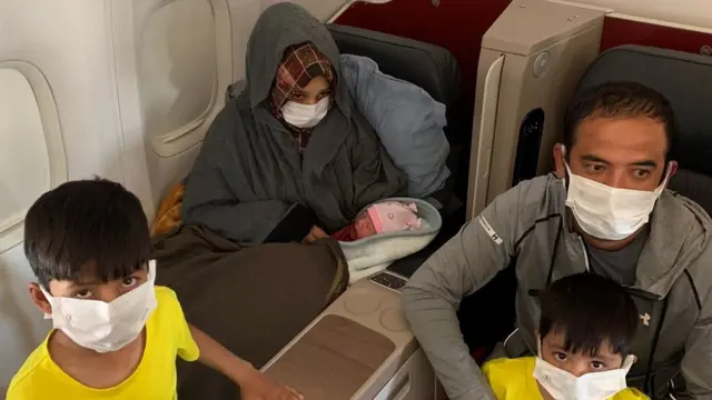 Soman Noori combet 365 não abrebebê no colco, ao lado do marido e dos dois filhos, dentro do avião