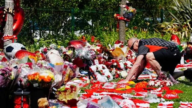 Un hombre arrodillado dejando un tributo en memoria de Diogo Jota