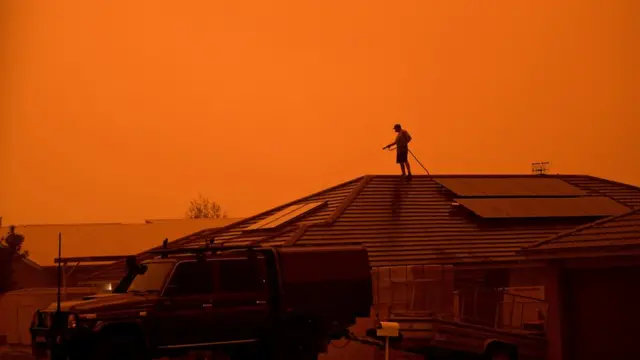 Um morador usa uma mangueirajogo foguete blazejardim para molhar a casa enquanto ventos fortes espalham fumaça e cinzas do incêndio que atinge Nova Gales do Sul, na Austrália