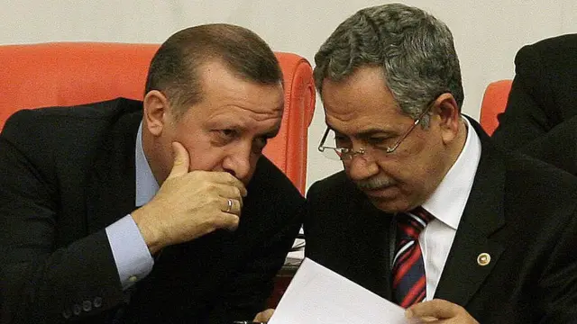 Dönemin Başbakanı Recep Tayyip Erdoğan ve TBMM Başkanı Bülent Arınç, 25 Şubat 2010'da TBMM'de yan yana otururken görülüyor. Erdoğan ağzını kapatarak Arınç'la konuşuyor. Arınç ise bir yandan dinlerken bir yandan da elindeki kağıtları inceliyor.