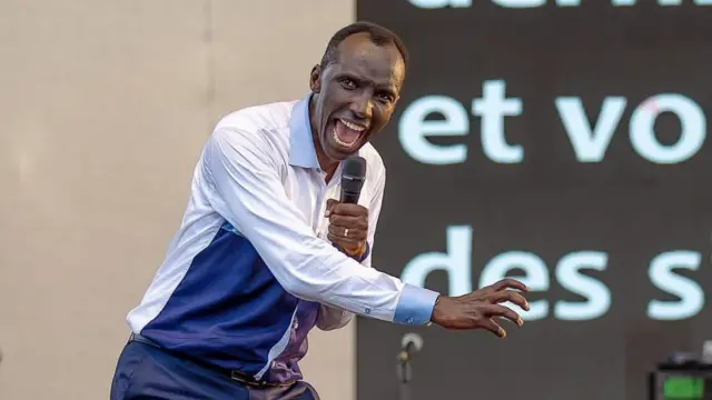 Chris Ndikumana mw'ishati ifise ibara ryera, iryirabura n'ubururu, mu kuboko kumwe afise 'micro', ariko aravuga ubutumwa (ifoto mbarankuru yo mu bubiko)