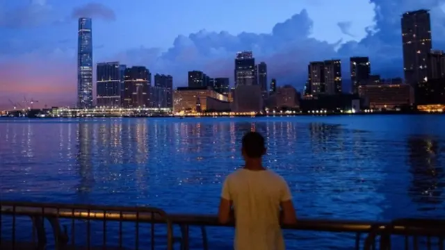 A man looks on as light pollution illuminates clouds above the Kowloon skyline in Hong Kong before sunrise on June 26, 2017.