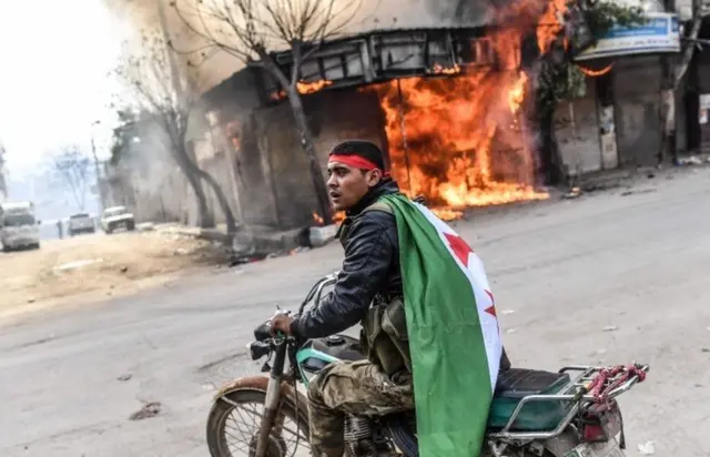 یکی از سربازان ارتش آزاد سوریه در مقابل مغازه در حال سوختن در عفرین