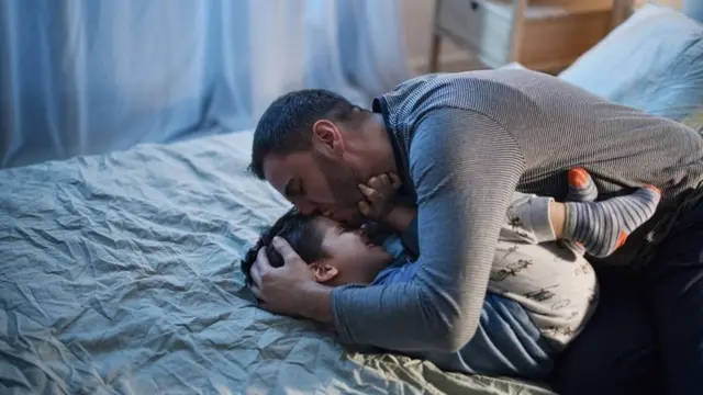 Un père embrasse son enfant couché sur le lit sur le front
