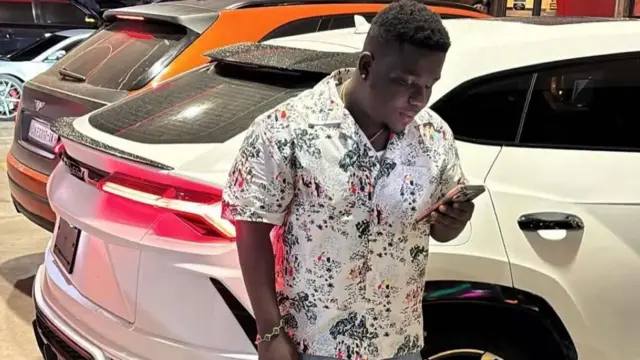 Abu Trica stand beside luxury car he display on his social media platforms 