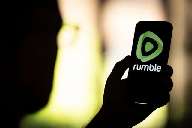 Mão segura celular com logo Rumble