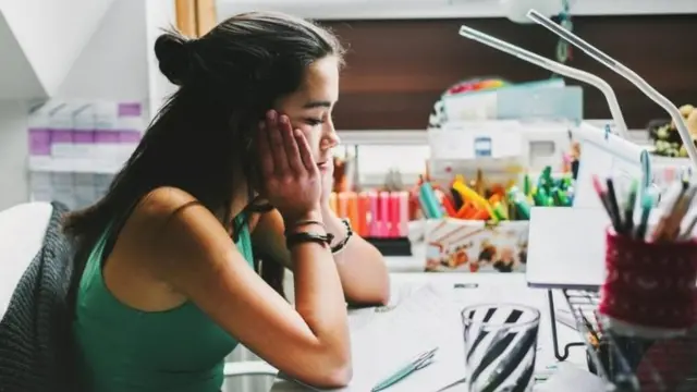 Une fille anxieuse devant une feuille et un stylo sur une table.