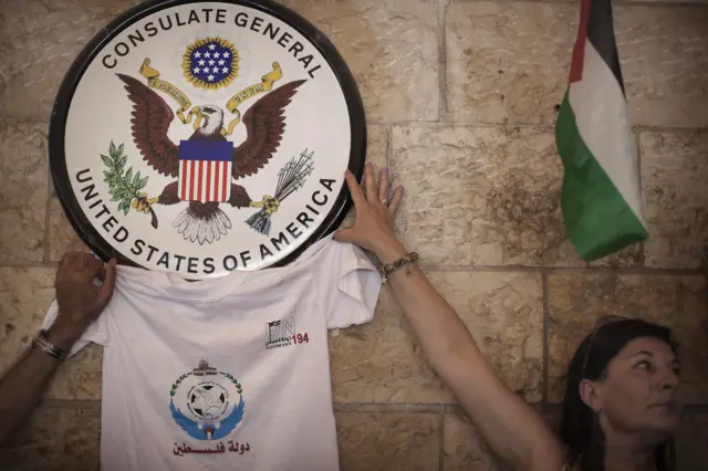 ناشطون فلسطينيون بجوار شعار القنصلية العامة الأمريكية في القدس، خلال احتجاج على تدخل الولايات المتحدة في محاولة الفلسطينيين الحصول على الاعتراف بدولتهم في الأمم المتحدة، في 21 سبتمبر/أيلول 2011