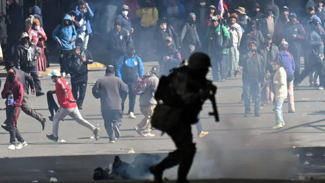 Um policial corre em frente a manifestantes durante uma marcha que pede a renúncia do presidente boliviano Rodrigo Paz, em meio ao agravamento da crise econômica e de combustíveis no país, devido à escassez de dólares americanos e à queda na produção interna de energia, em La Paz, Bolívia, 25 de maio de 2026