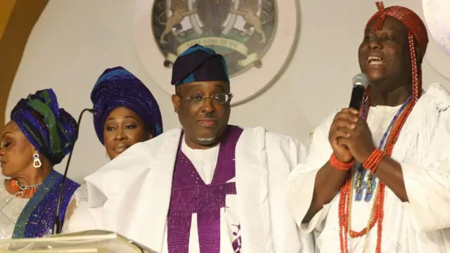 Ọọni Adeyeye Ogunwusi wọ asọ funfun, de ade sori, o si fi ilẹkẹ sọrun, awọn ọmọ ọba Ọọni Okunade Sijuwade duro tii, awọn naa wọ asọ funfun, wọn de fila olomi buluu sori.