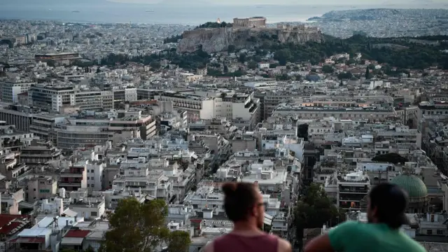 Young men sit at on a hill overlooking the city of Athens, 8 August 2018
